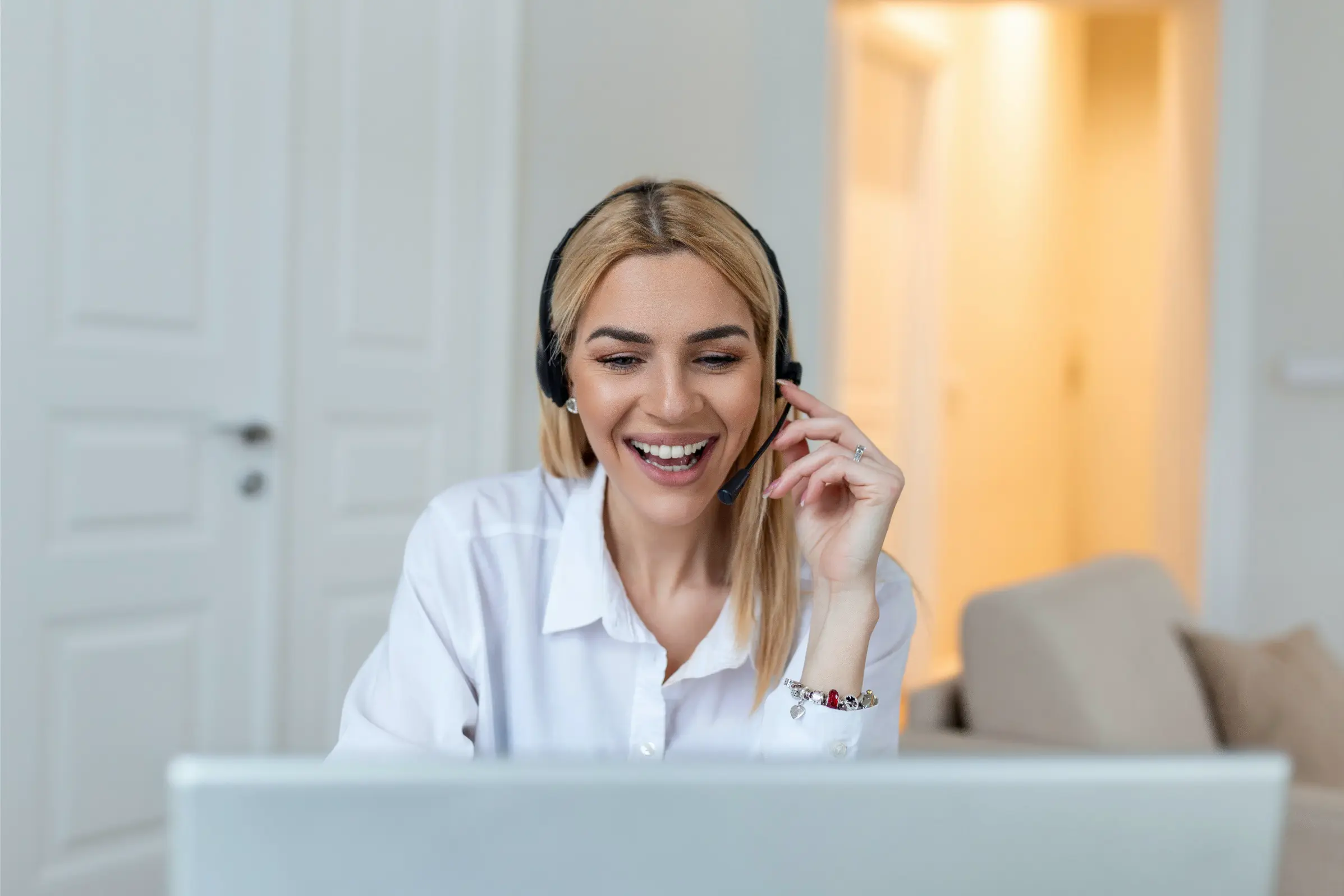 a smiling customer support agent with headset works on computer while supporting a customer on a phone call